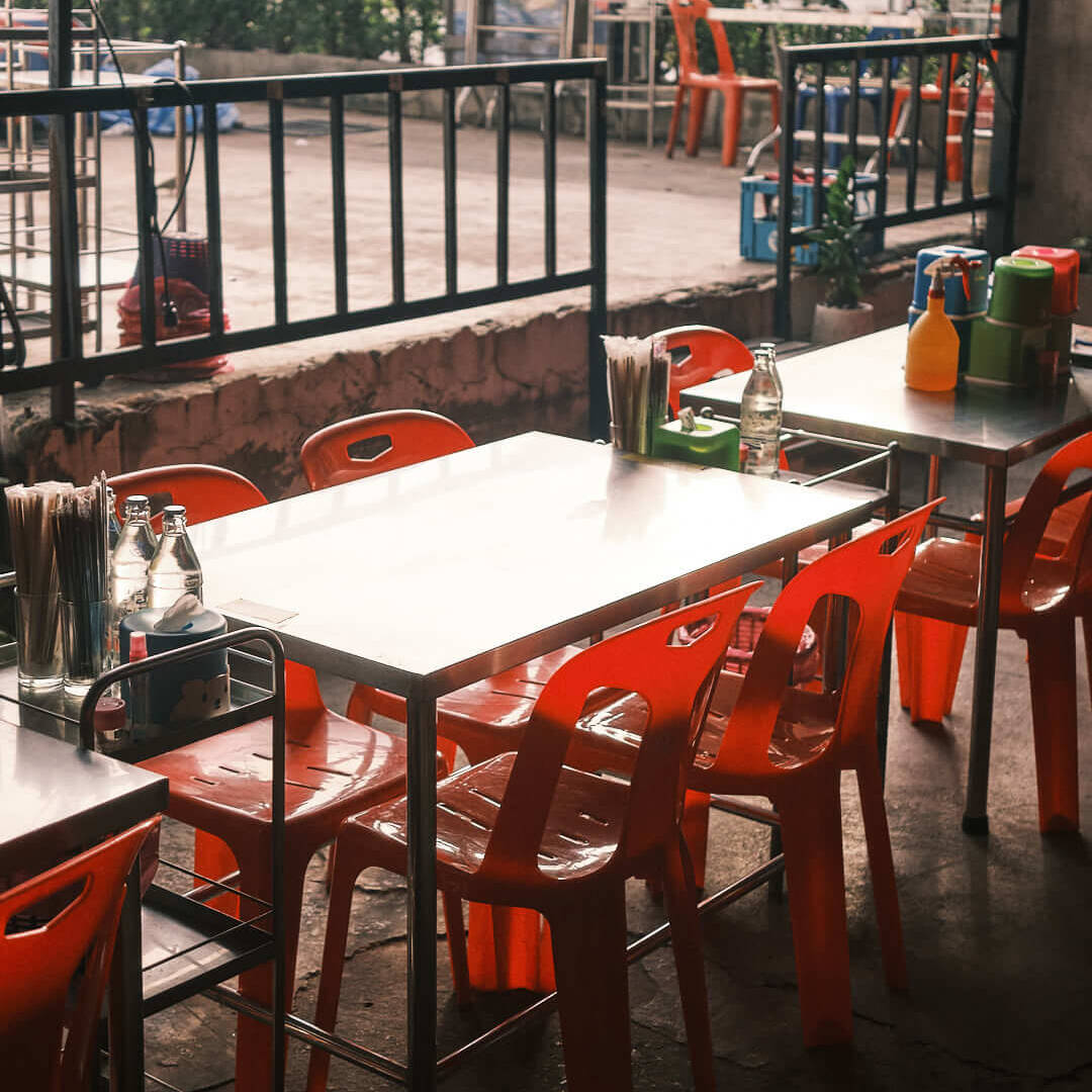 A cozy street-side eatery in Bangkok with bright orange chairs and tables, showcasing the city's vibrant street food culture.