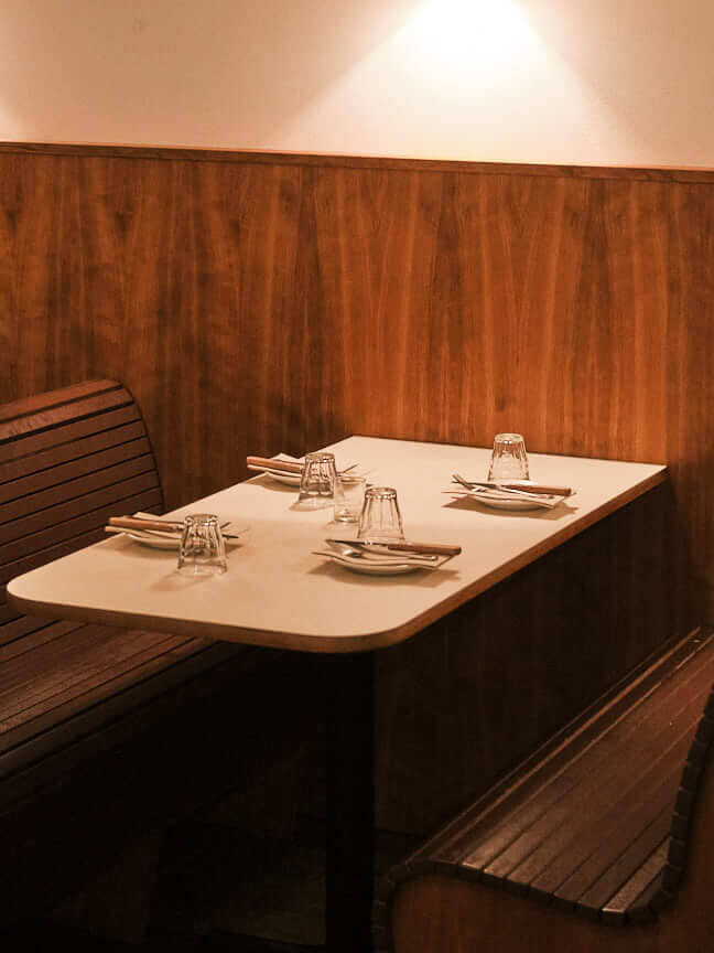Cozy booth seating at Bertie Berlin, featuring polished wooden paneling, soft ambient lighting, and minimalist table settings. Captures the intimate and stylish New York-inspired dining atmosphere in this Berlin restaurant. Perfect for restaurant photography and showcasing modern interior design.