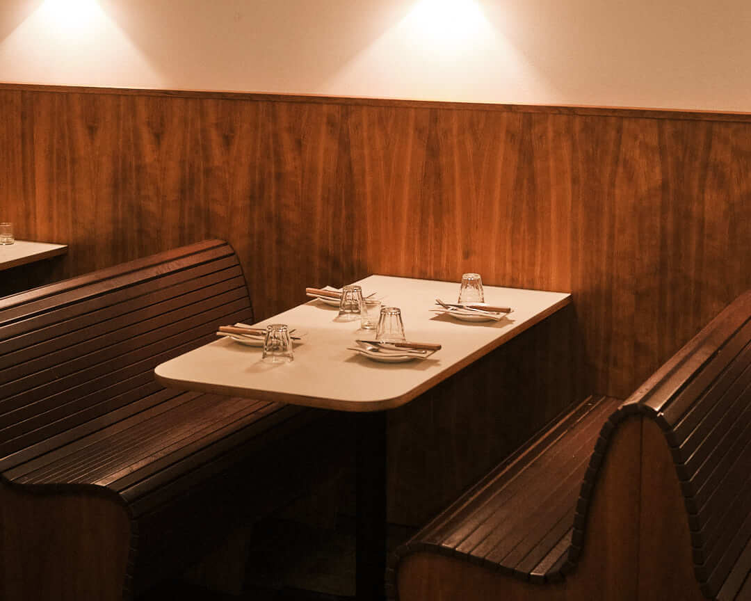 Cozy booth seating at Bertie Berlin, featuring polished wooden paneling, soft ambient lighting, and minimalist table settings. Captures the intimate and stylish New York-inspired dining atmosphere in this Berlin restaurant. Perfect for restaurant photography and showcasing modern interior design.