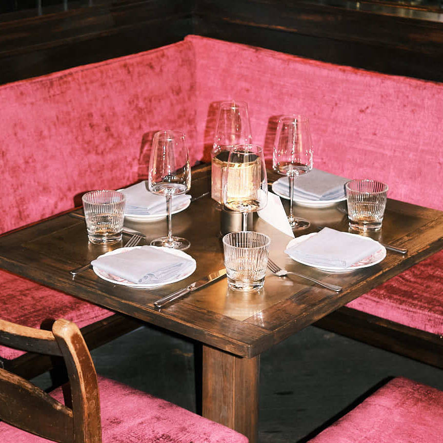 Elegant dining setup at Clärchens Ballhaus in Berlin, featuring a cozy corner with vibrant pink velvet seating, fine glassware, and warm ambient lighting. This photo captures the restaurant’s refined yet inviting atmosphere, perfect for enjoying traditional German cuisine.