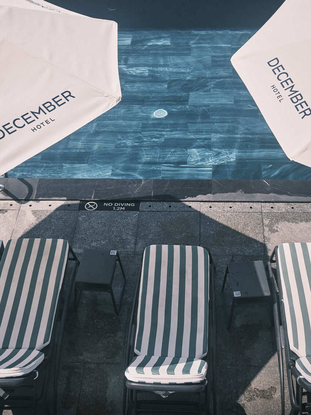 December Hotel’s infinity pool under clear skies, bordered by elegant striped umbrellas and lounge chairs, delivering a sophisticated and relaxing environment.