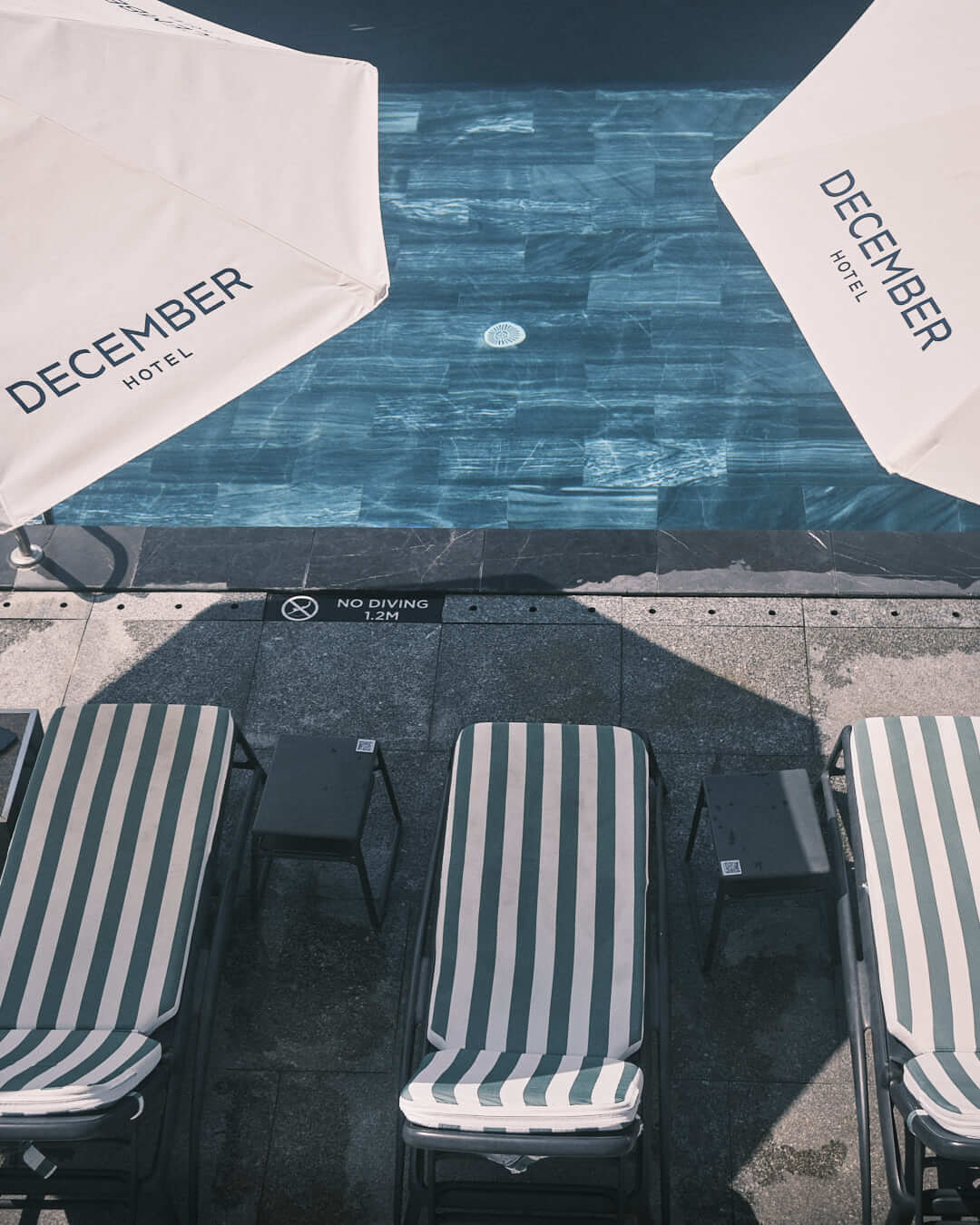 December Hotel’s infinity pool under clear skies, bordered by elegant striped umbrellas and lounge chairs, delivering a sophisticated and relaxing environment.