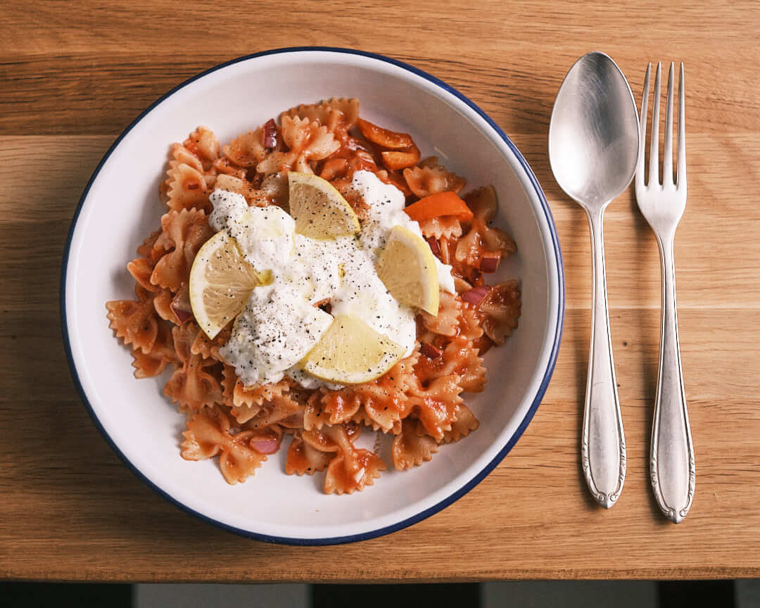 Delicious bowl of farfalle pasta topped with fresh lemon slices, creamy sauce, and cracked black pepper on a wooden table, showcasing vibrant colors and textures. A perfect example of professional food photography highlighting culinary details.