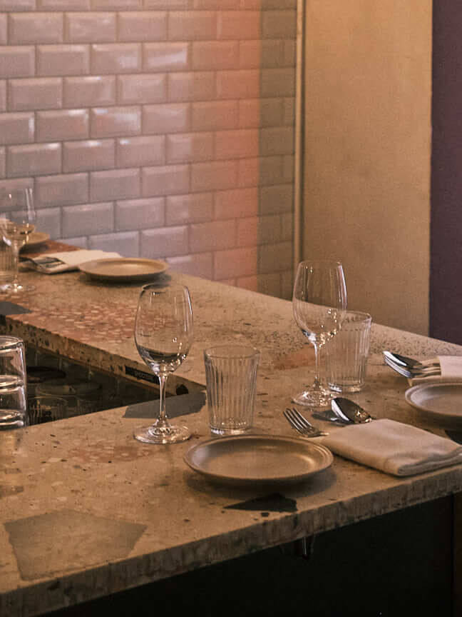 A cozy bar setup at La Côte Restaurant in Berlin, showcasing elegant glassware and neatly arranged plates on a terrazzo-style countertop, capturing the inviting and warm atmosphere of the restaurant.