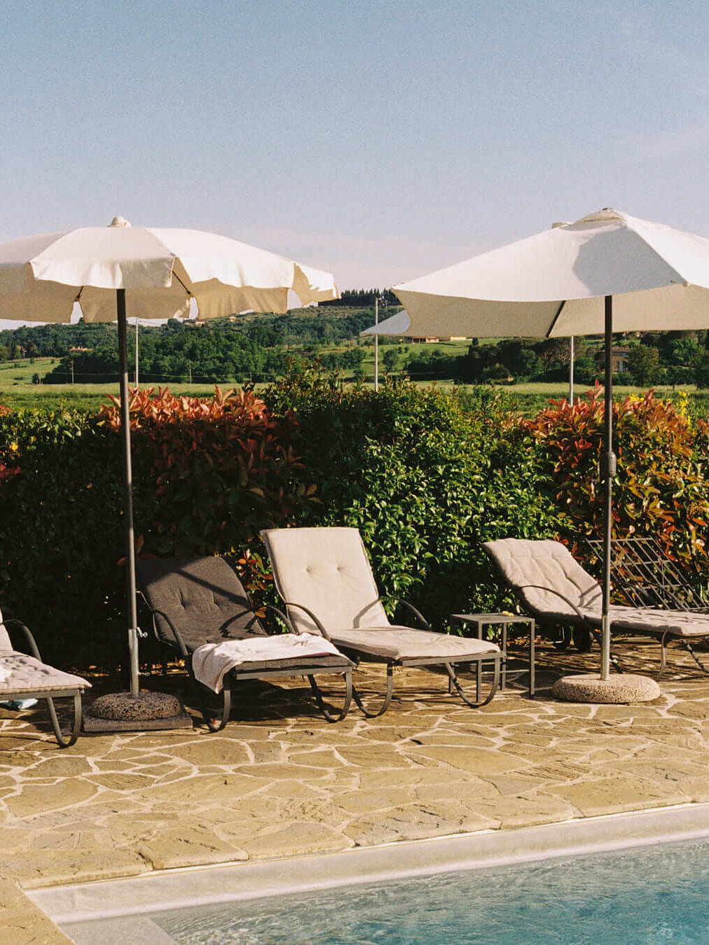 Poolside chairs shaded by elegant umbrellas with rolling Tuscan hills in the background, showcasing a relaxing retreat amidst nature.