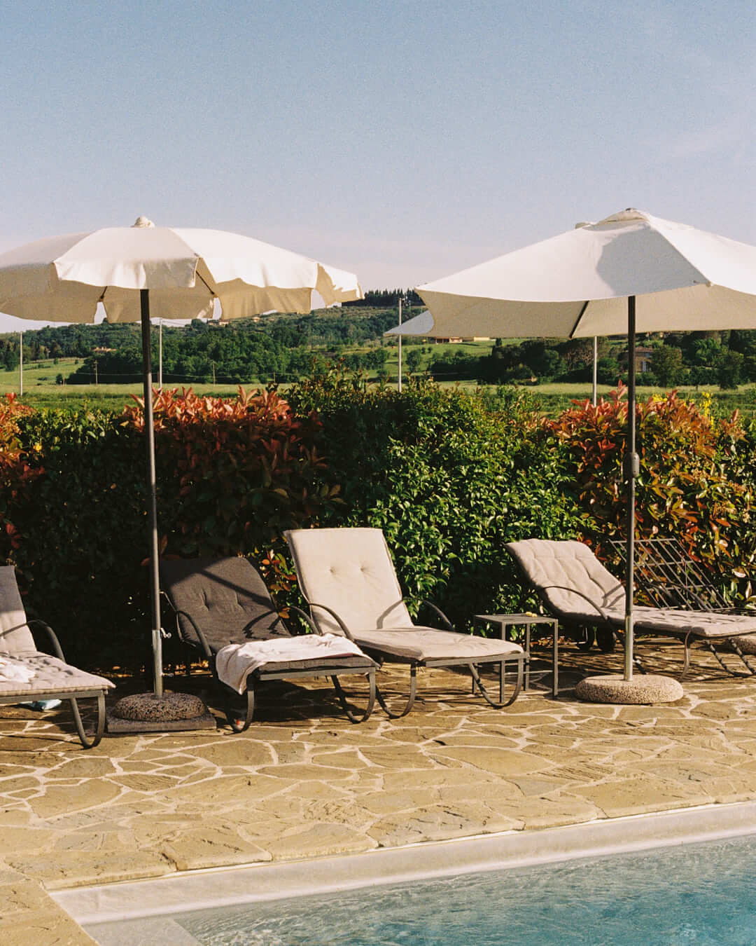 Poolside chairs shaded by elegant umbrellas with rolling Tuscan hills in the background, showcasing a relaxing retreat amidst nature.