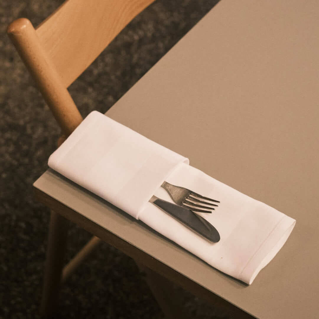 Another close-up of a minimalist table setting at Klinke Berlin, showcasing folded napkins and utensils on a gray tabletop. An inviting dining space in Berlin for enjoying German tapas.
