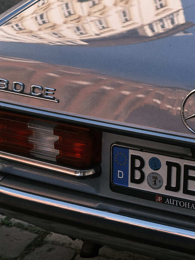 A beautifully maintained red Mercedes-Benz 230 CE with reflections accentuating its polished finish.