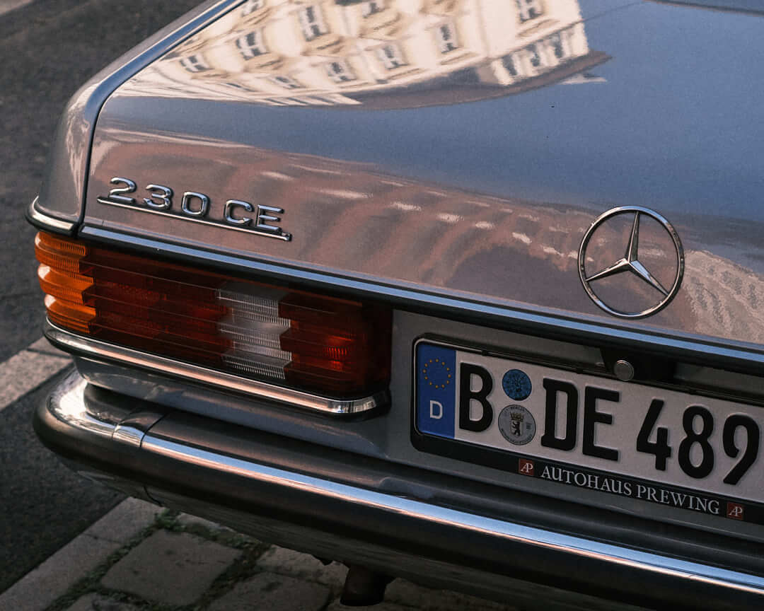 A beautifully maintained red Mercedes-Benz 230 CE with reflections accentuating its polished finish.