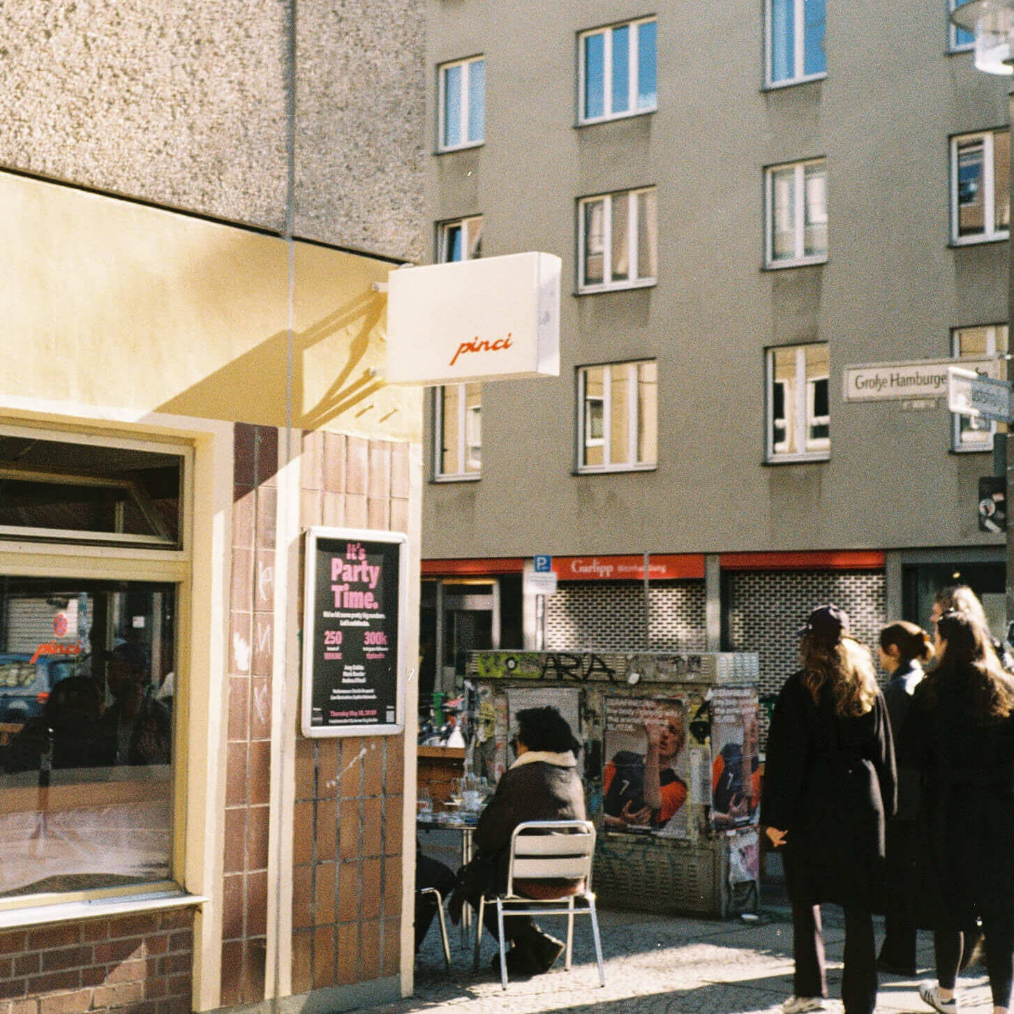 A sunny street corner view of Pinci restaurant in Berlin-Mitte, showing a white minimalist lightbox sign with the red text 