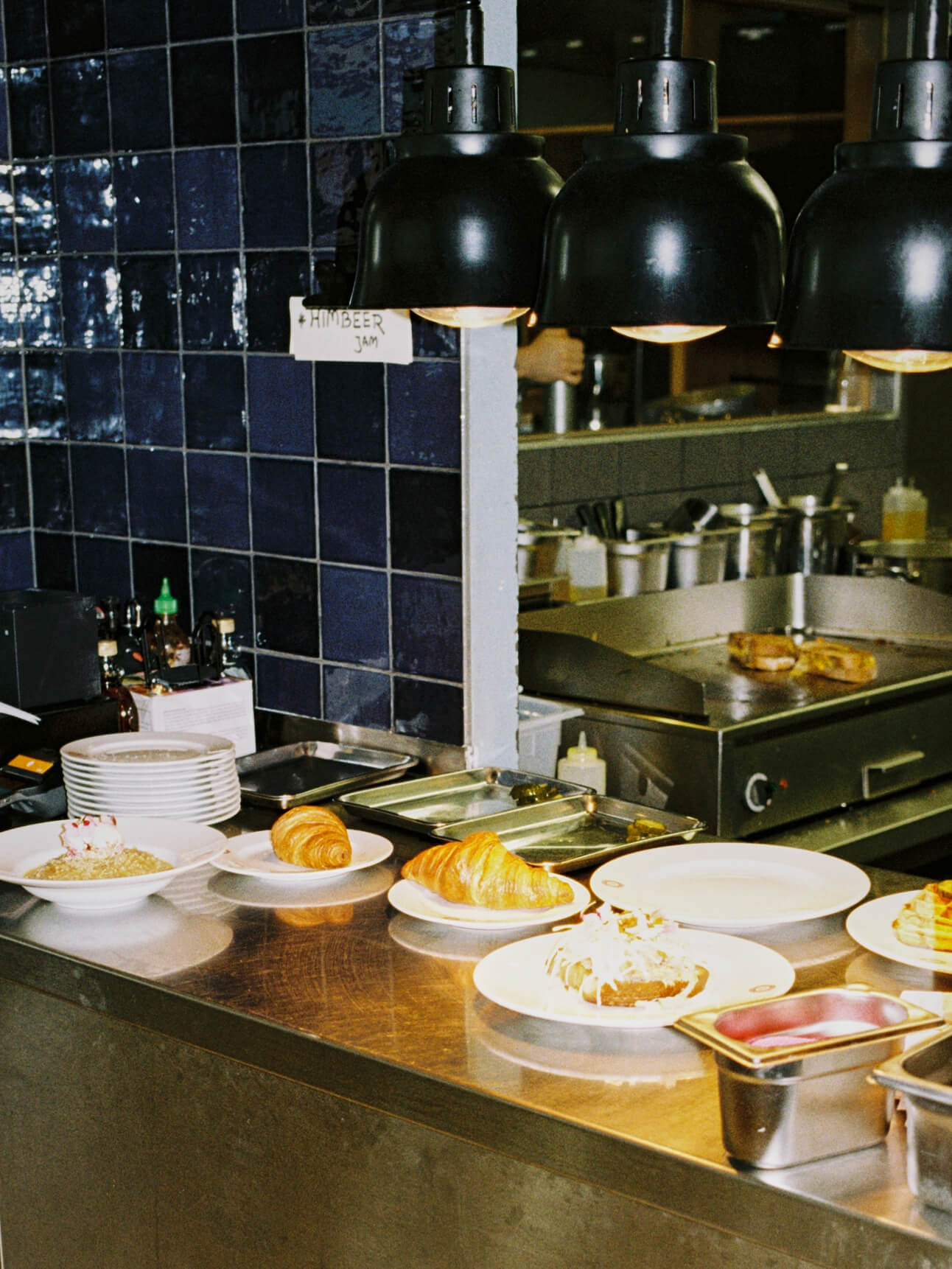 Open kitchen pass at Frühstück 3000 showing freshly baked croissants and breakfast plates under heating lamps.
