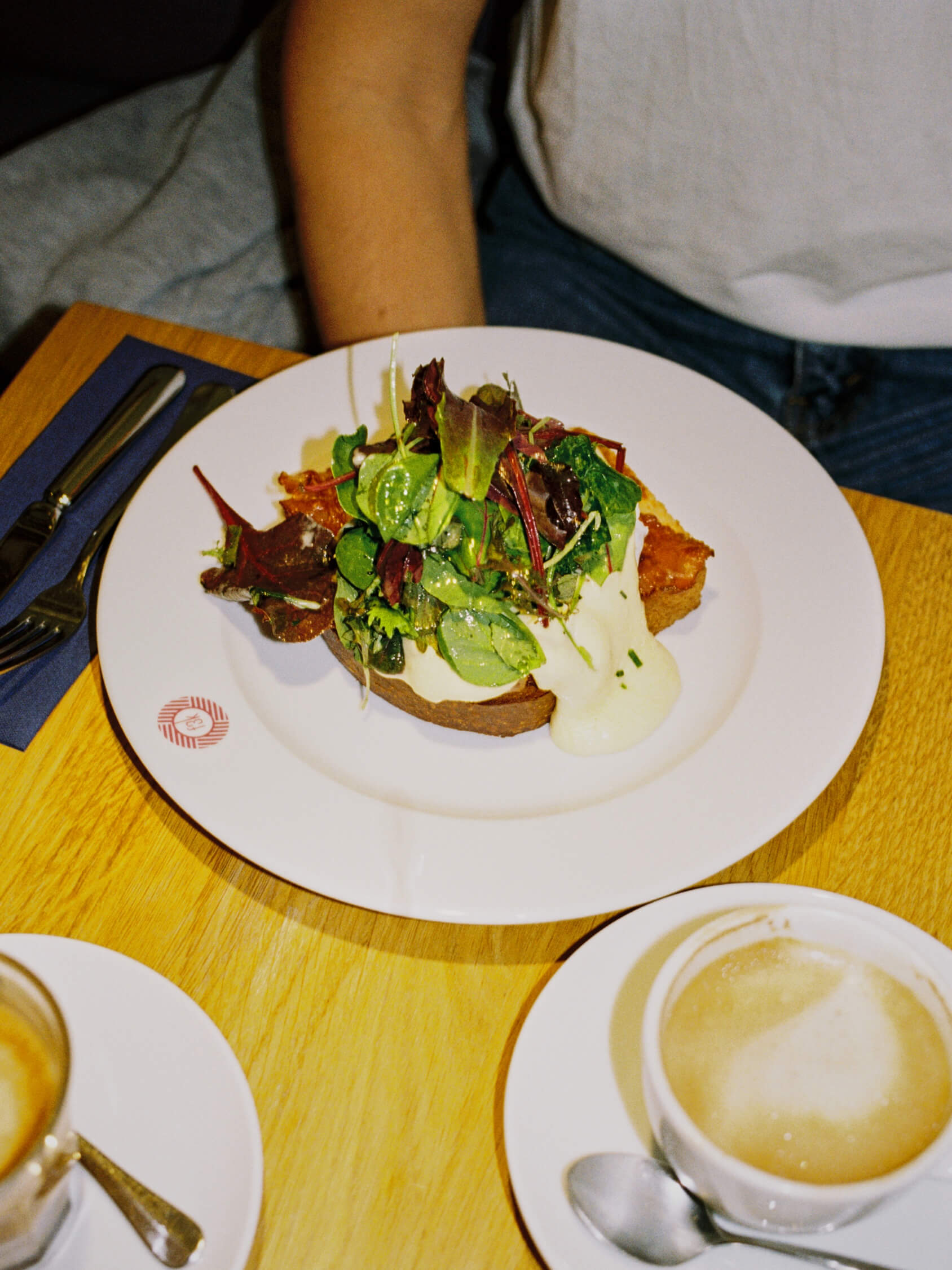 Top-down film photo of gourmet egg toast with greens and a cappuccino at Frühstück 3000 Berlin.