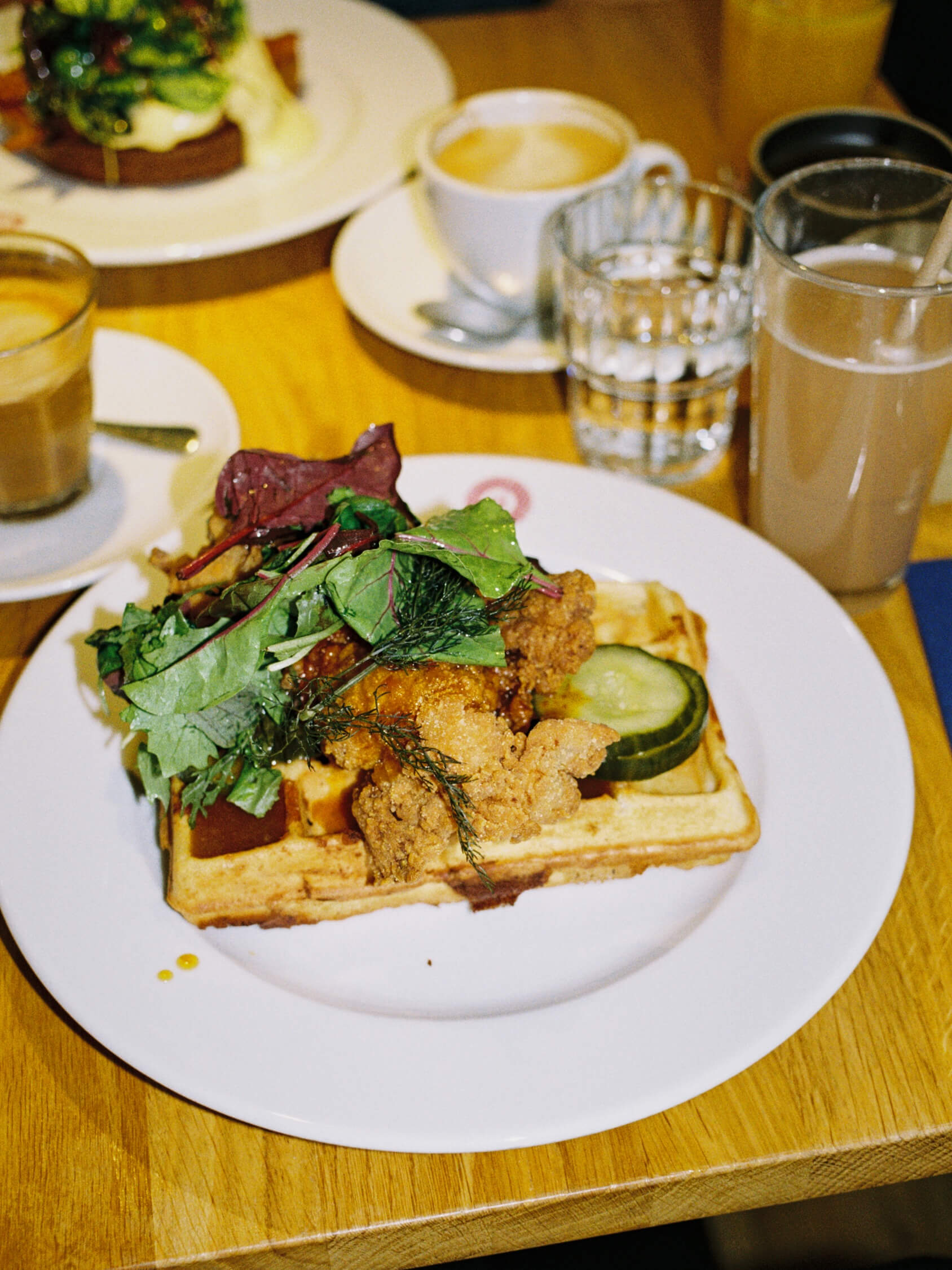 Close-up 35mm photograph of chicken and waffles on a wooden table at a Berlin brunch cafe.