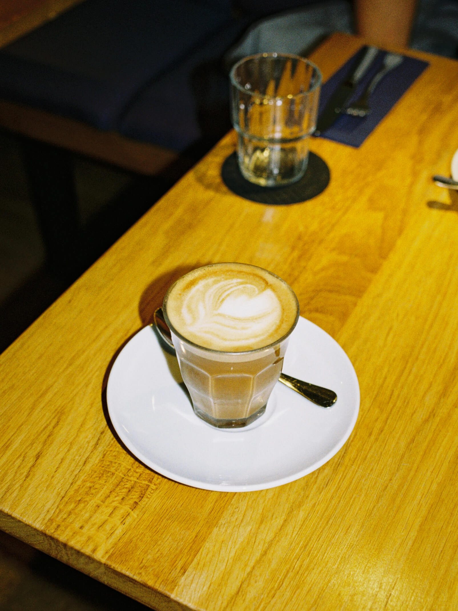 Flat white coffee with delicate latte art served in a glass on a wooden table, shot on analog film.