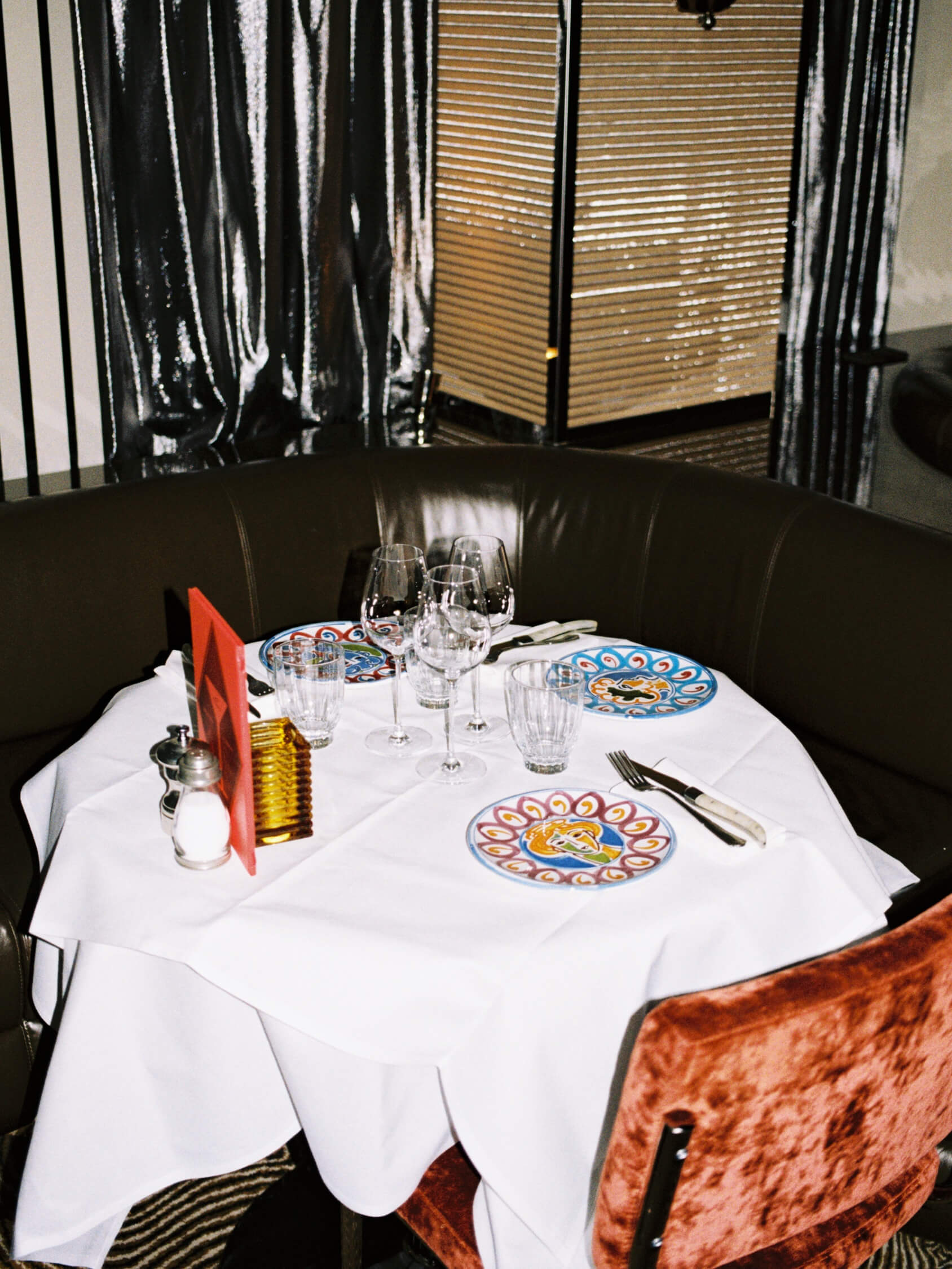 Cozy circular leather booth and mirrored table set with wine glasses inside Pamela restaurant in Berlin, shot on 35mm film.