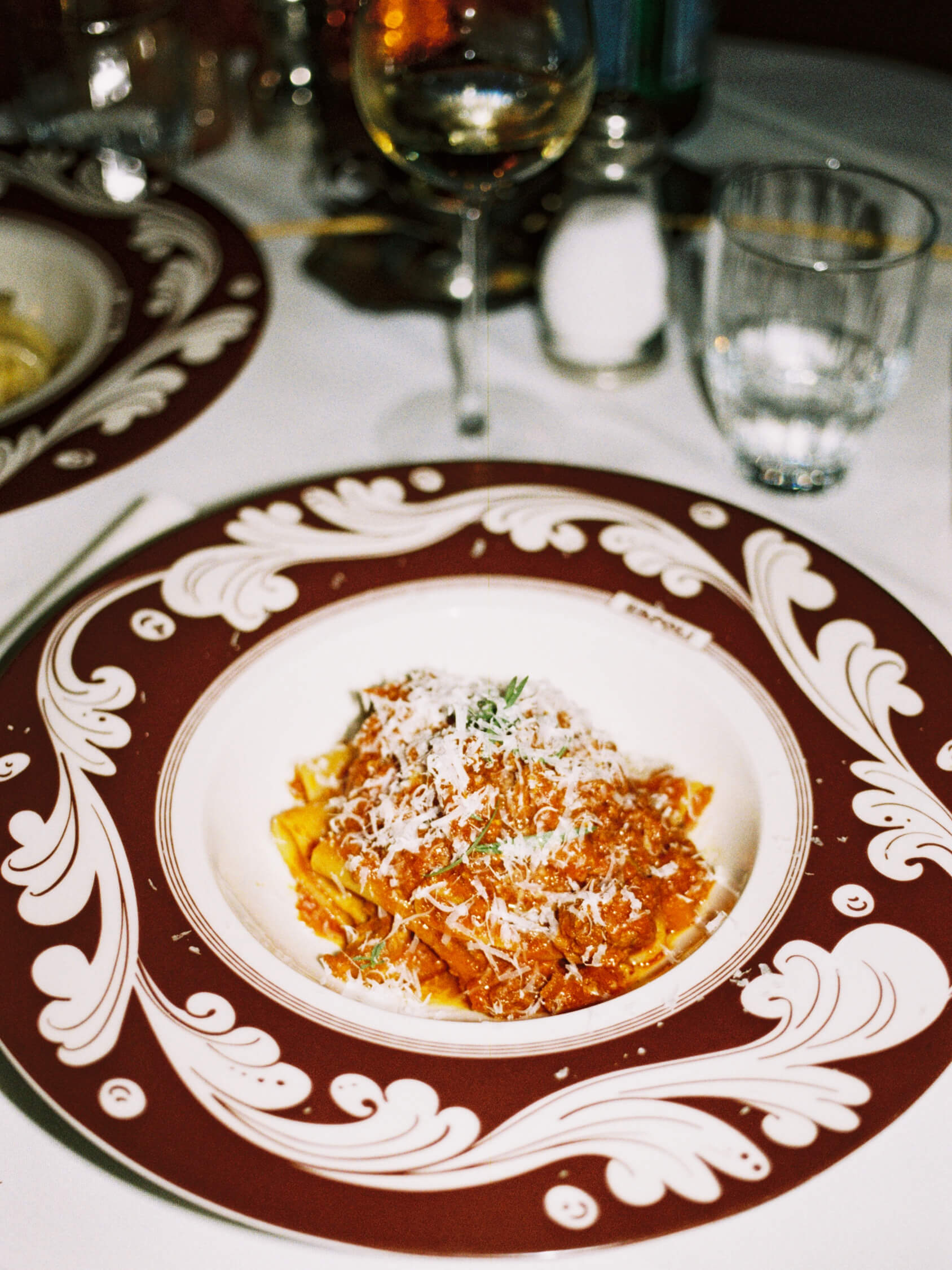 Rich ragù pasta topped with shredded parmesan in a decorative red ceramic bowl at Pamela restaurant in Berlin, shot on 35mm film.