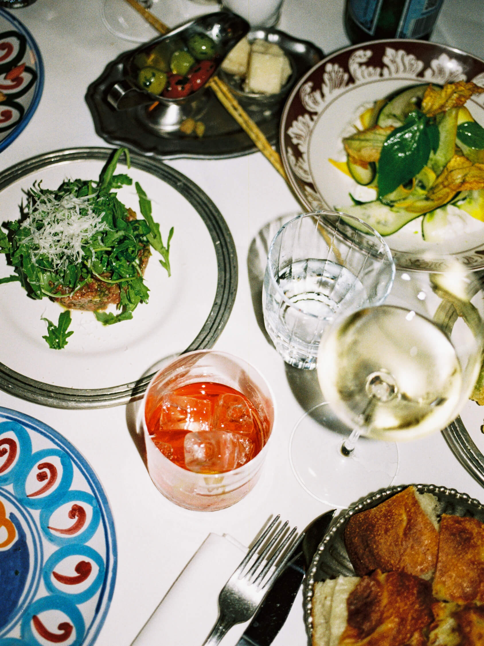 Top-down 35mm film photo of an Italian dinner spread with beef tartar, cocktails, and wine at Pamela in Berlin.