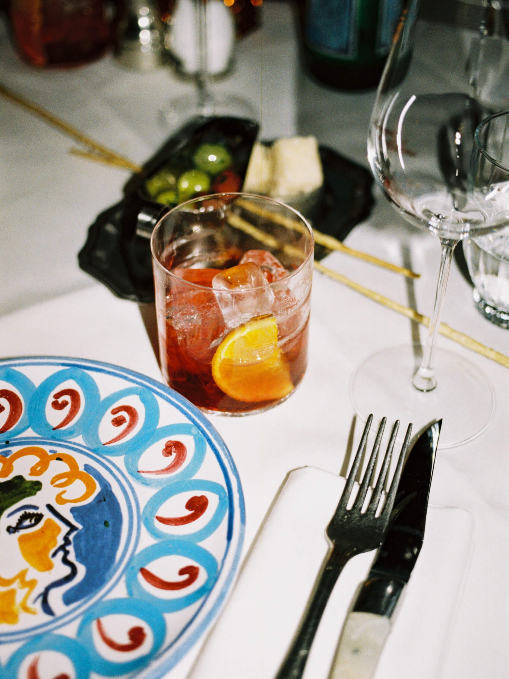 Negroni cocktail with orange slice on a white tablecloth next to vintage Italian ceramic plate at Pamela Berlin.